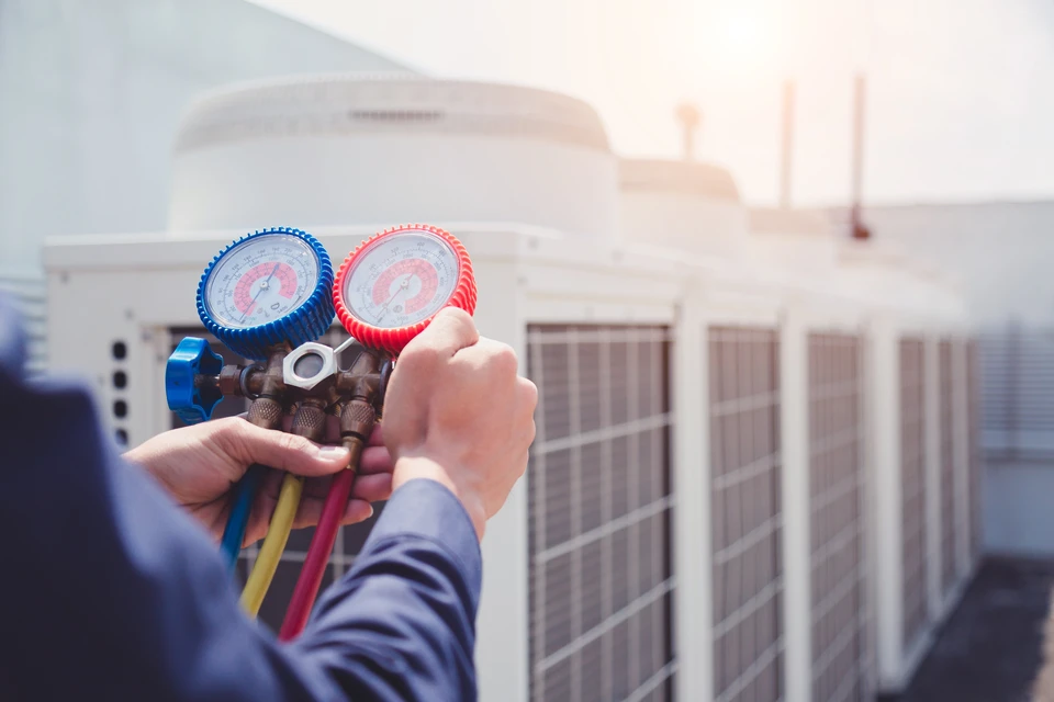 Technicien en climatisation tenant des manomètres à l'extérieur devant une unité de climatisation résidentielle