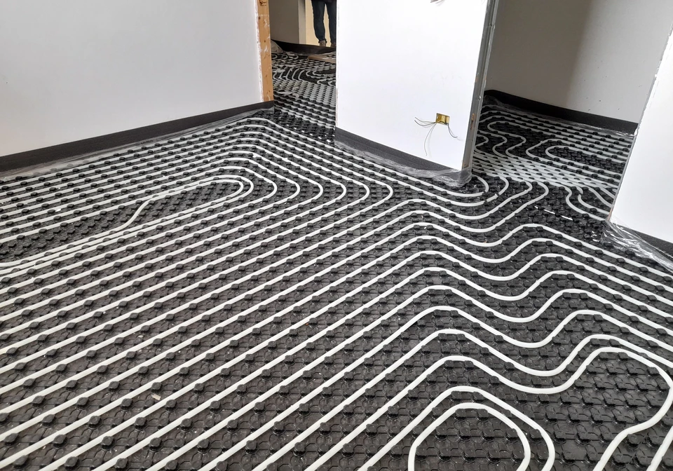 Un plombier professionnel travaille sur une installation de chauffage au sol dans un local technique