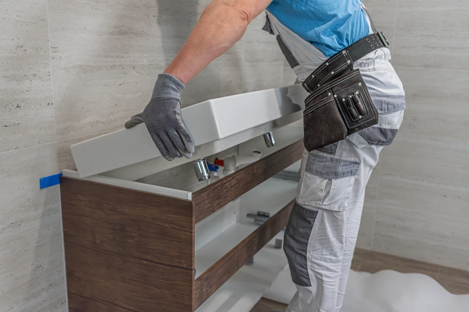 Salle de bain moderne avec vasque blanche posée sur plan de travail en pierre claire et meuble bas en bois naturel
