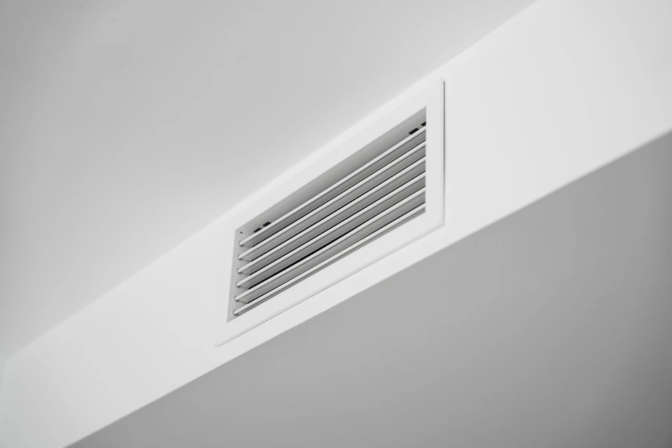 Installateur en gants de protection blancs et bleus positionnant une grille d'aération ventilation dans plafond blanc d'intérieur résidentiel