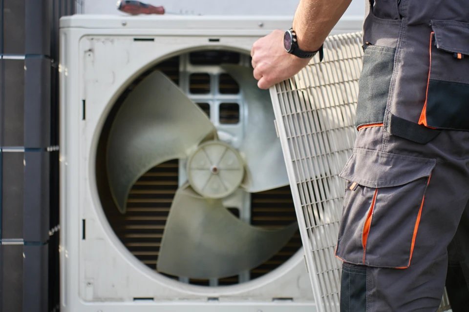 Technicien en équipement de protection individuelle installant une unité de climatisation extérieure sur façade résidentielle