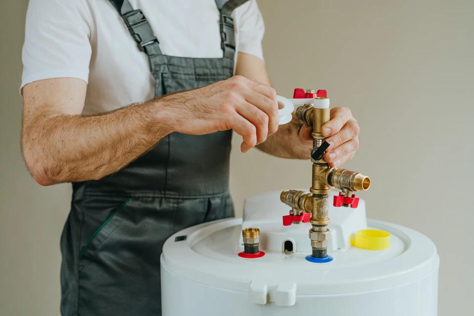 Plombier professionnel effectuant la maintenance d'un chauffe-eau électrique dans un sous-sol résidentiel