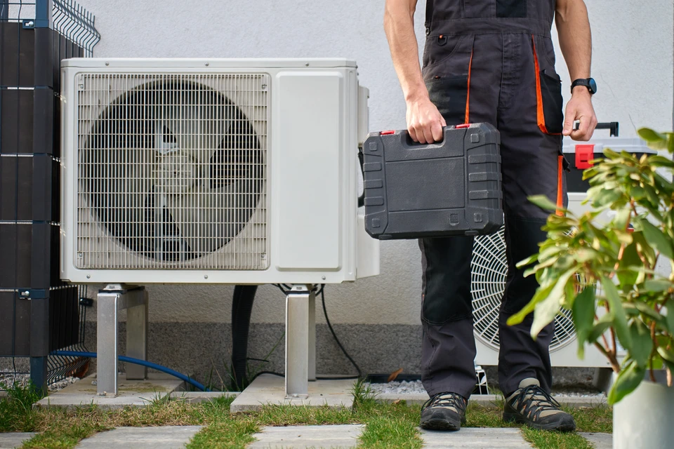 Technicien effectuant la maintenance d'un climatiseur mural intérieur, les mains positionnées pour retirer ou installer le filtre à air