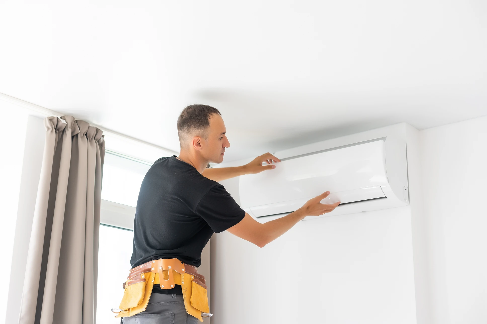 Technicien en uniforme rouge travaillant sur une unité de climatisation extérieure dans un environnement résidentiel avec panneaux solaires visibles sur toiture