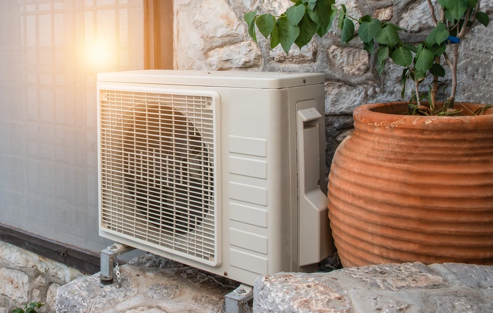 Technicien en salopette bleue installant un radiateur blanc près d'une fenêtre dans une pièce aux murs blancs